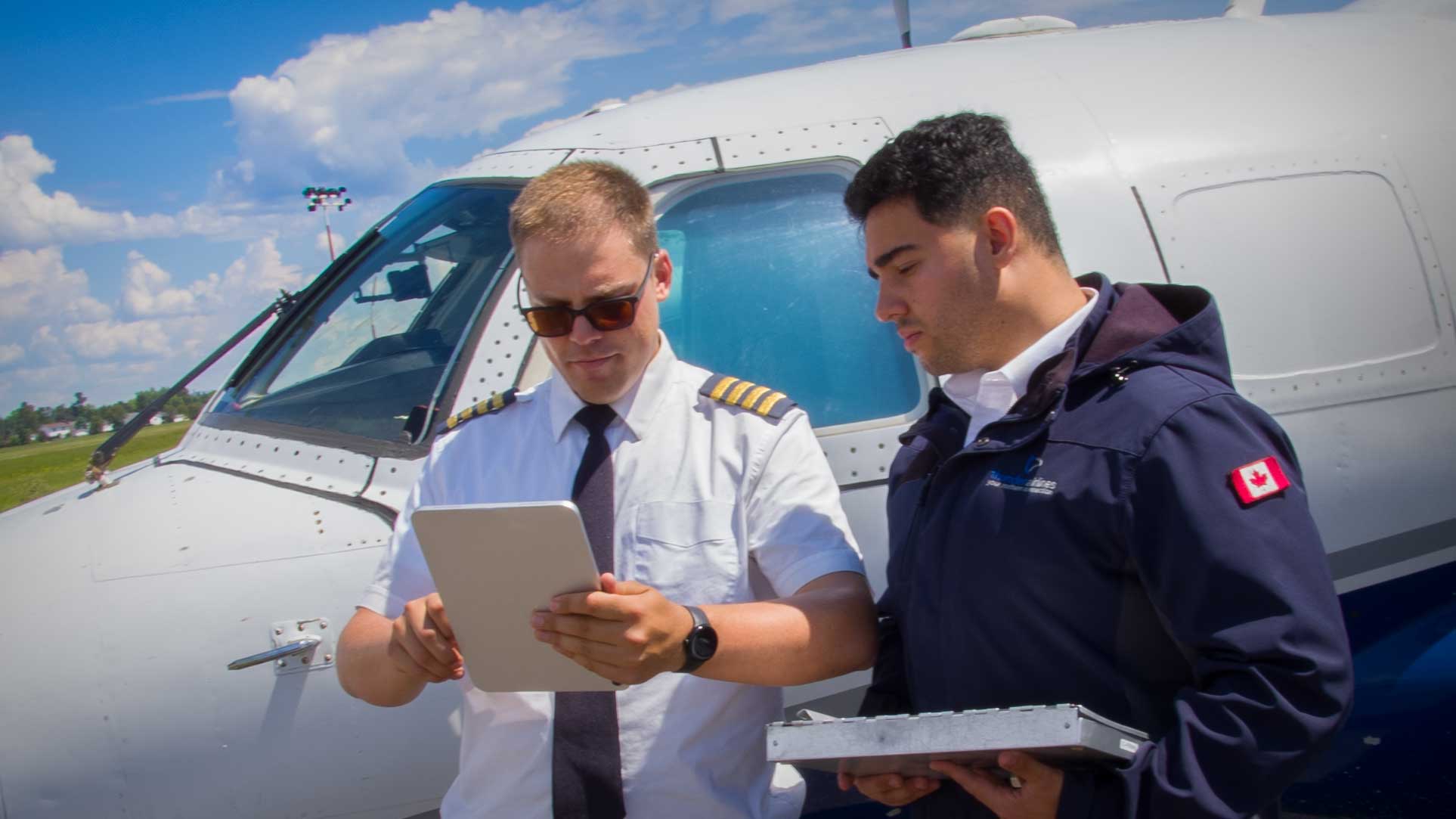 Two pilots in front of a plane looking at a tablet.